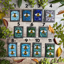 Mosaic bee art pieces on a wooden surface with leaves around